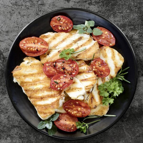 Halloumi cheese, grilled, with roasted cherry tomates and herbs. Top view over dark slate.